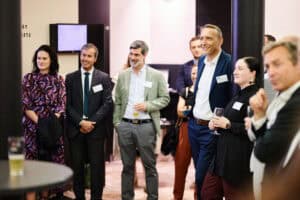 Business professionals at a conference or networking event in a modern indoor setting.