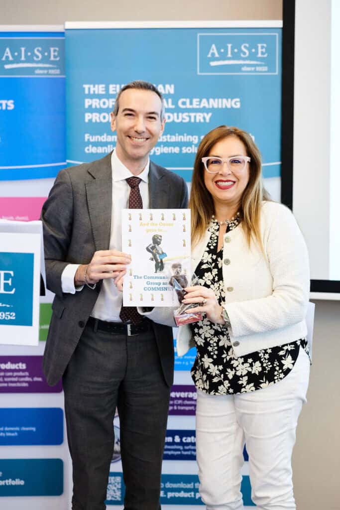 A professional setting with two smiling individuals holding a publication at a cleaning industry eve.