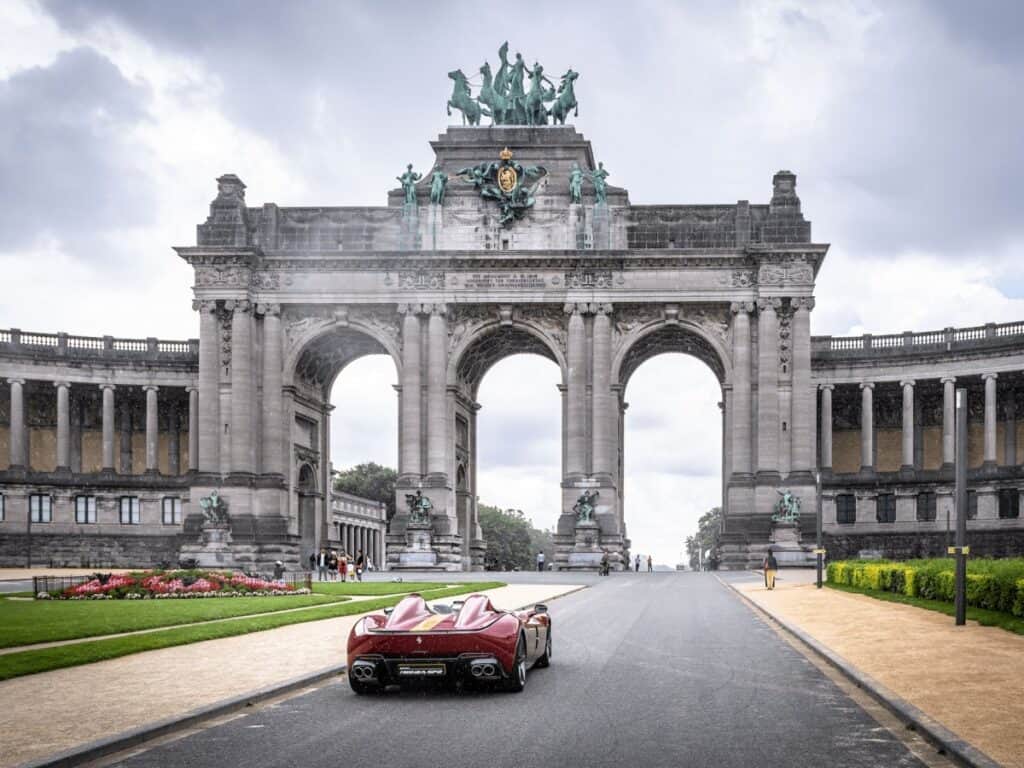 A car driving under a historic arch monument in a city setting.