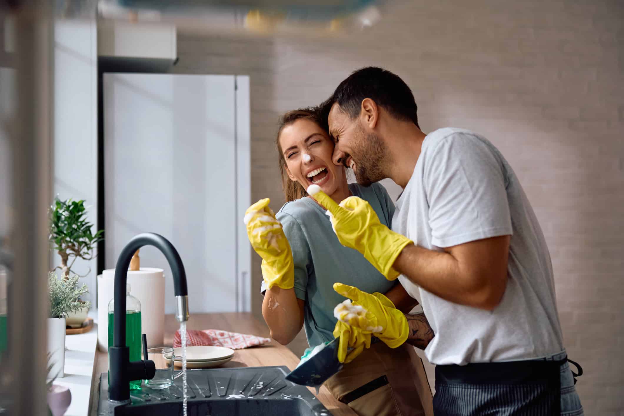 Playful couple having fun while doing the dishes in the kitchen.