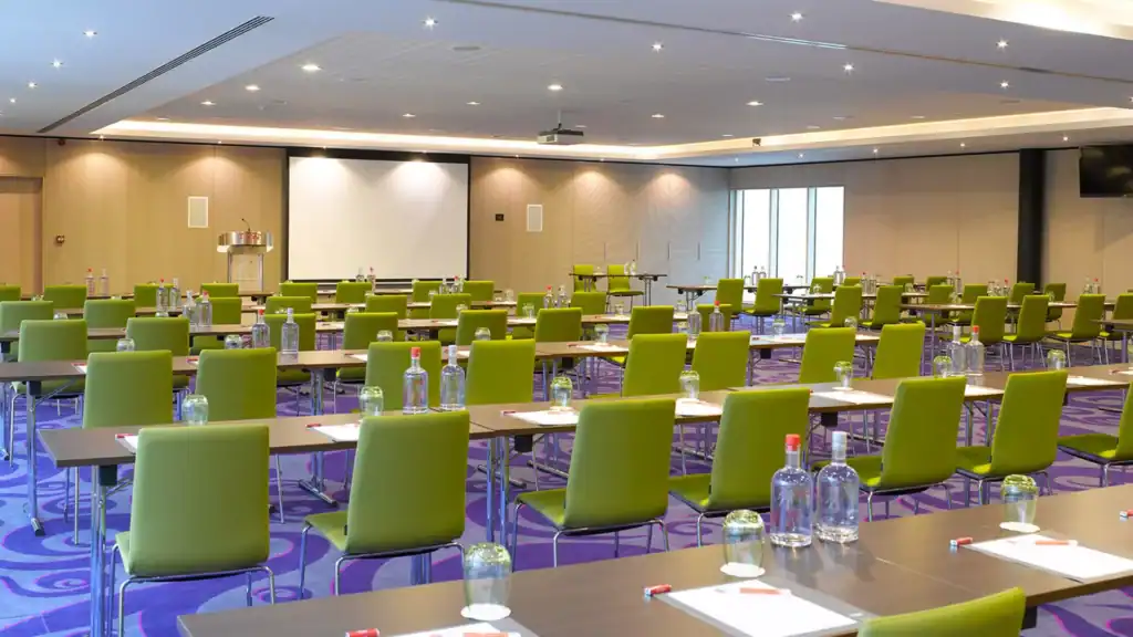 Modern conference room with green chairs, tables set with water bottles and notepads, ready for a co.