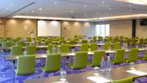 Modern conference room with green chairs, tables set with water bottles and notepads, ready for a co.